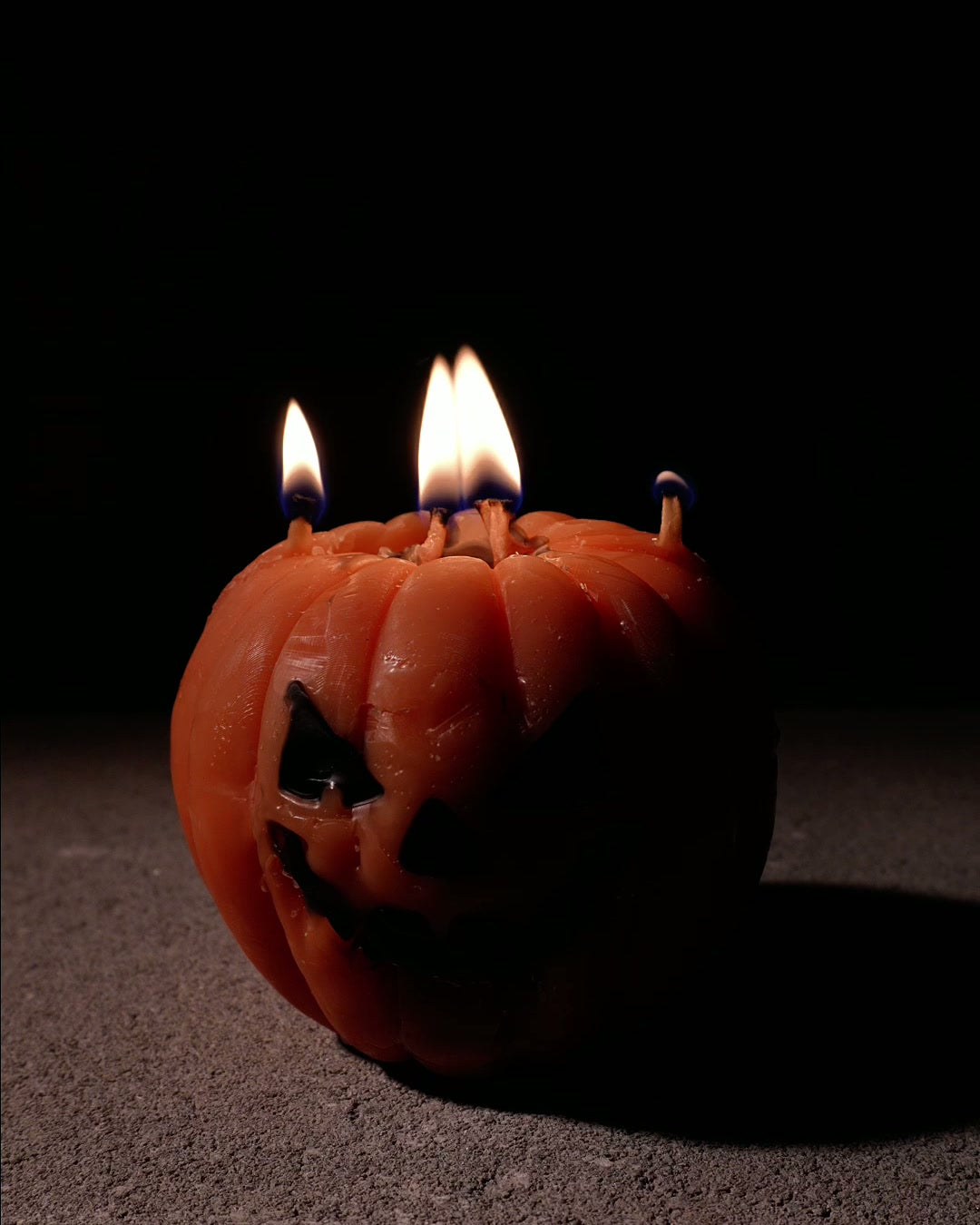 Memento Pumpkin candle lit, a wax jack-o'-lantern with four flames